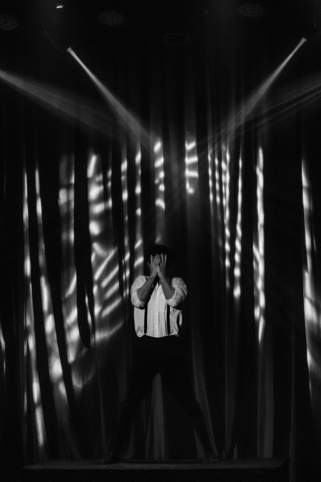 En blanco y negro: un actor se tapa la cara bajo un gobo de franjas de luz.