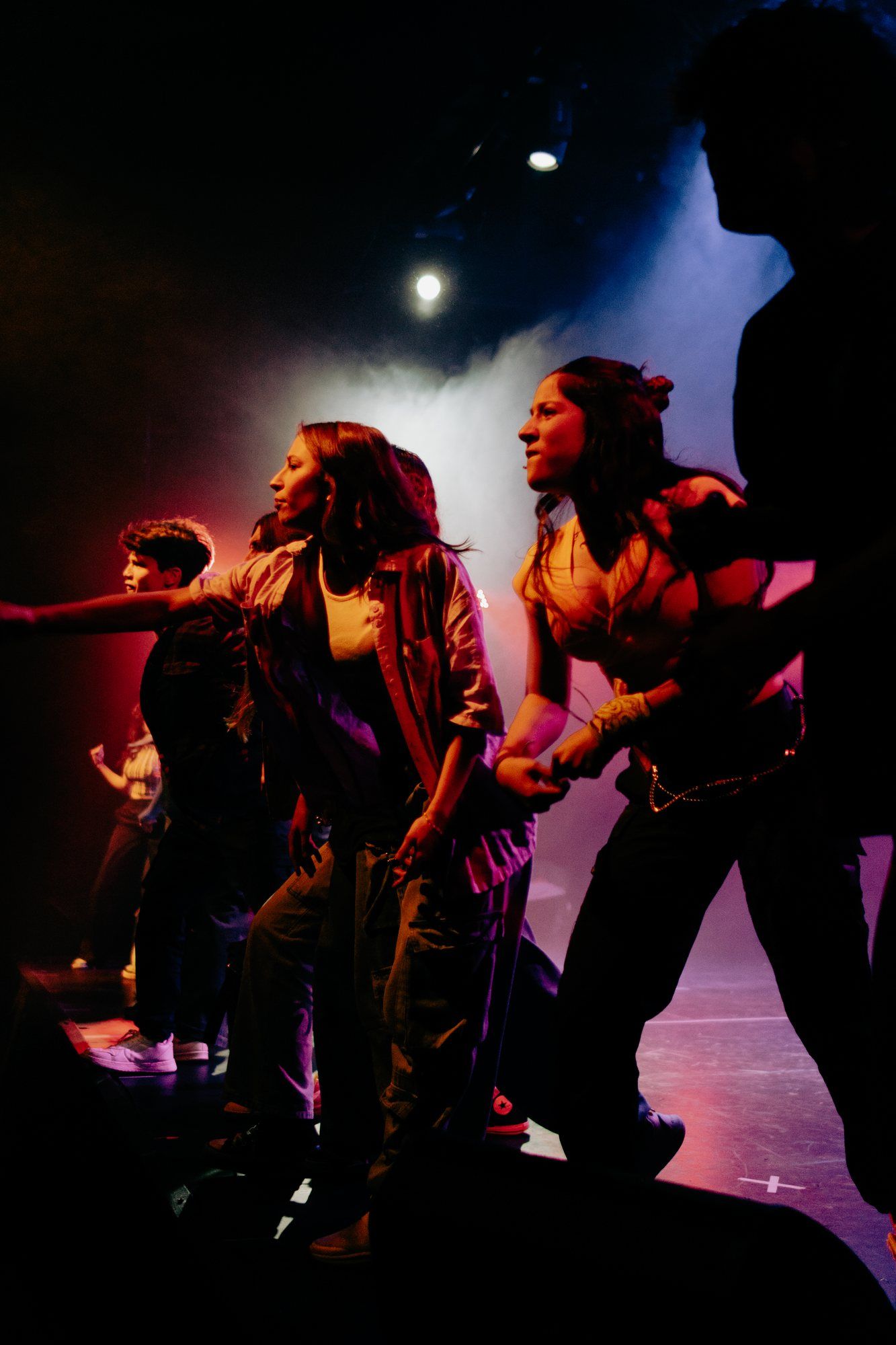Coreografía con luces rojas y violetas, vista desde un costado del escenario.