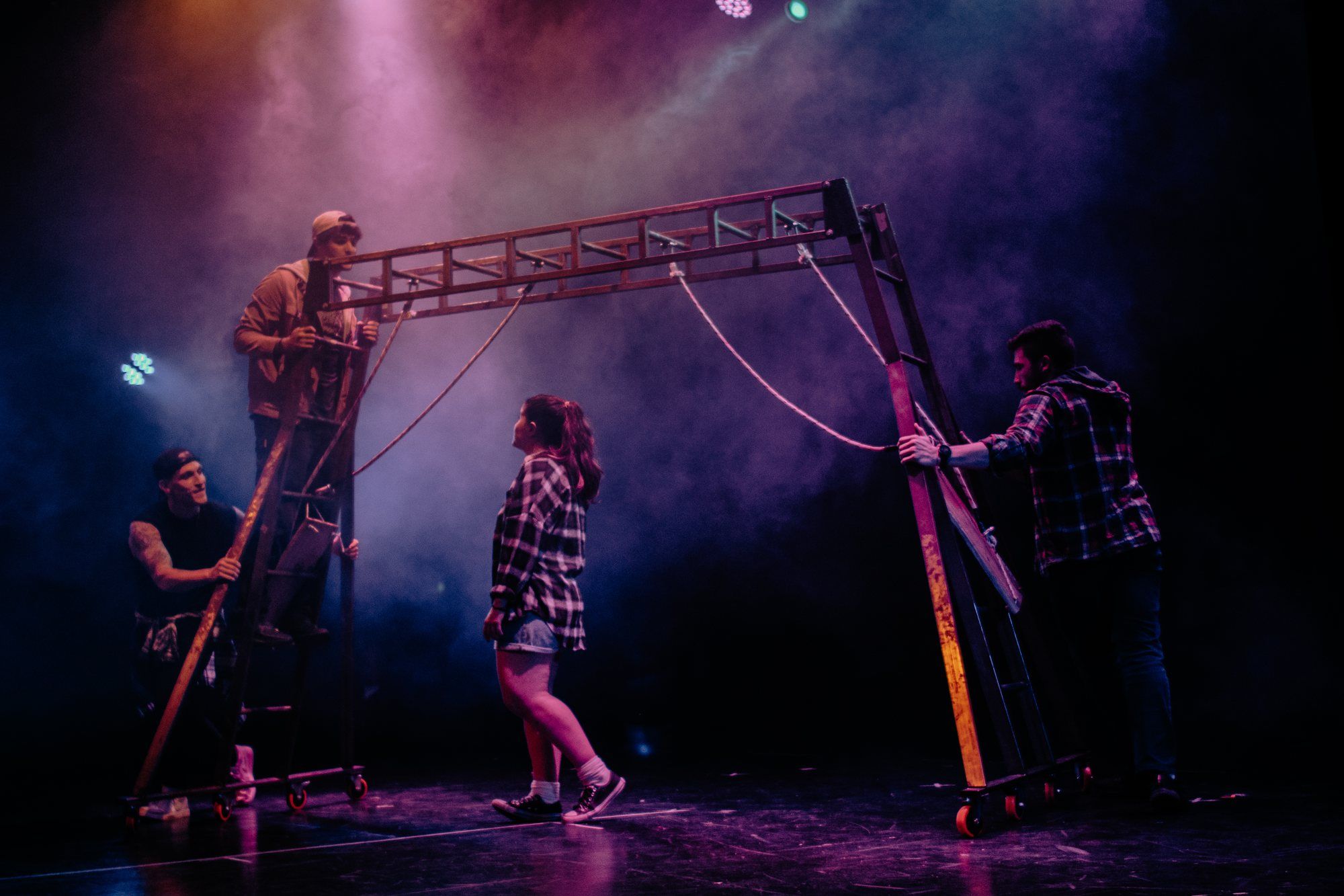 Estructura de escenografía con luz violeta y un intérprete trepando.